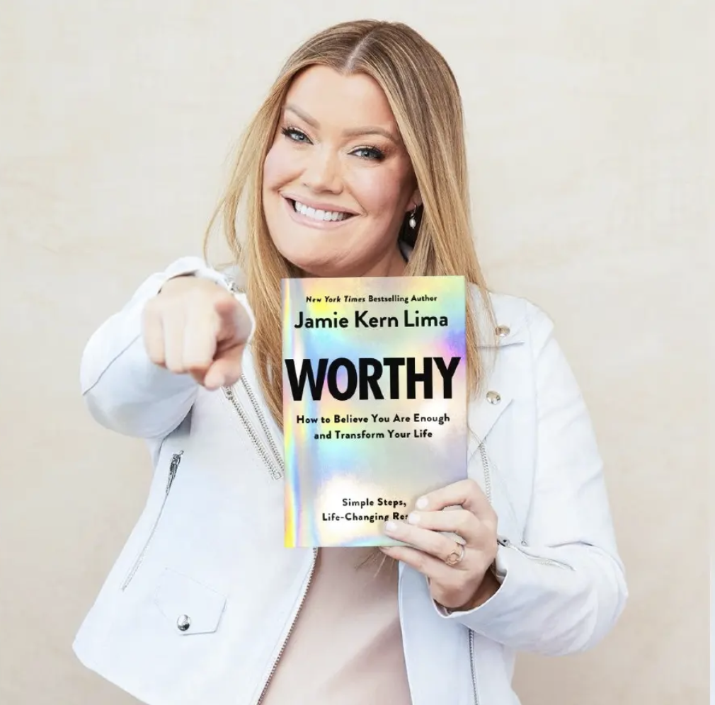 Jamie Kern Lima holding her book Worthy and pointing at the camera while looking straight at it. Self-worth.